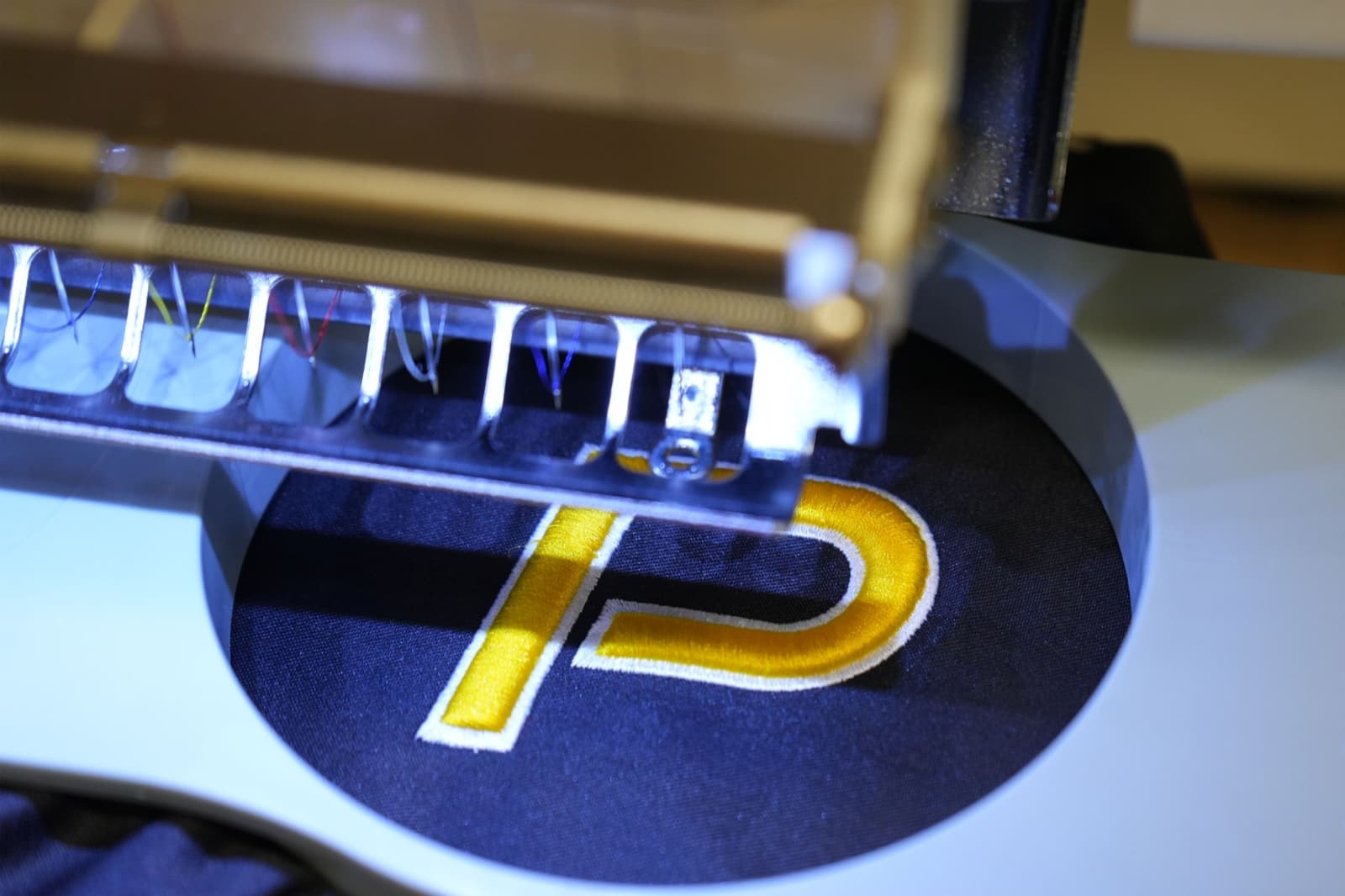 Commercial embroidery needle mid-stroke stitching through fabric