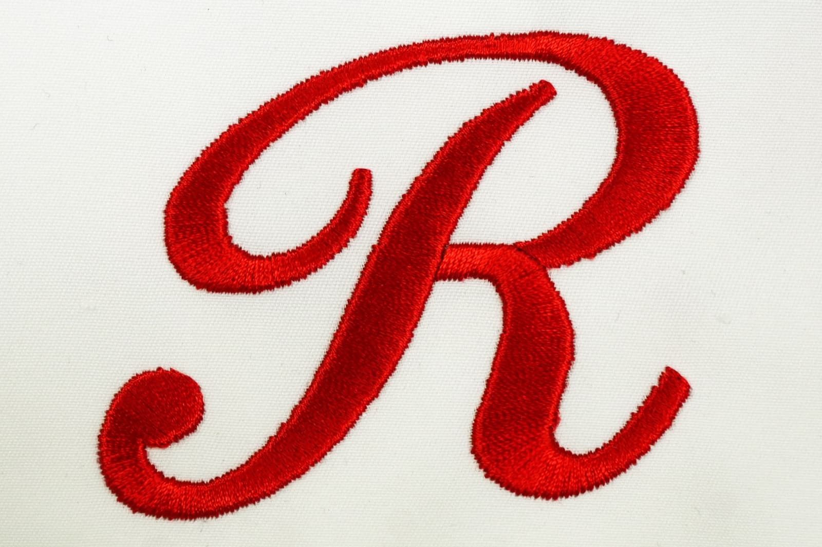Macro close-up of cursive script letter in satin stitch showing thread sheen